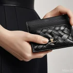 보테가 베네타의 카드홀더와 미니 지갑 비교 - **Prompt:** A close-up shot of a person's hands gently holding a classic black Bottega Veneta Intrec...